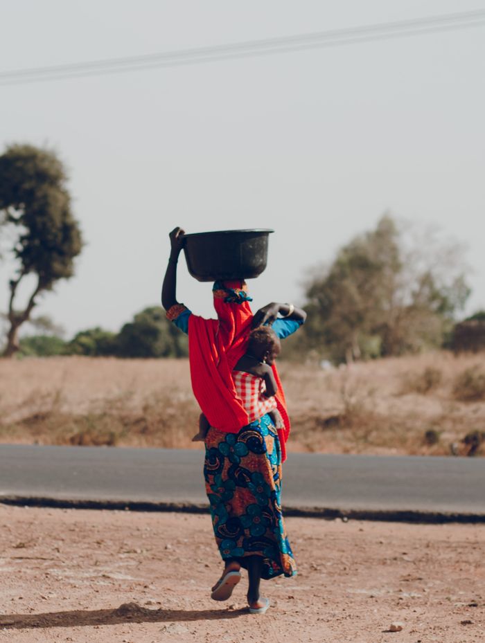 A woman carrying a child and a basin on her head, walking along a road.